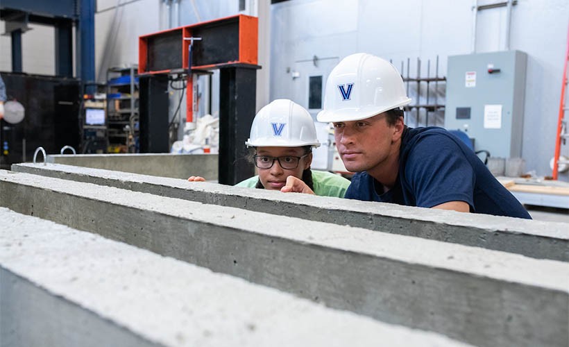 A professor and student wearing Villanova hardhats in the structures lab