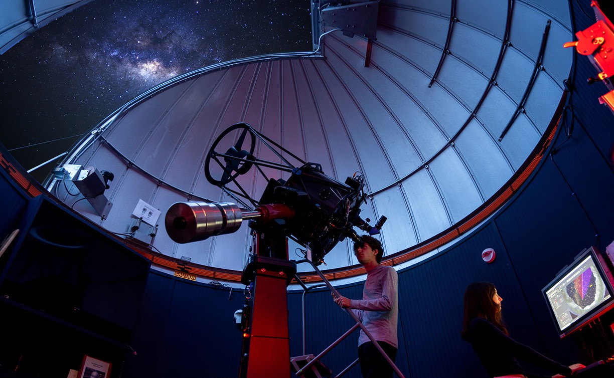 A student in the astronomy observatory looks into the night sky through a telescope.