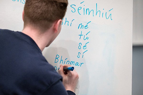 A student writes Gaelic on the whiteboard.