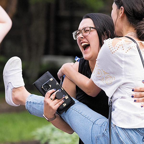 a young laughing woman has her hands full while lifting her female friend off the ground