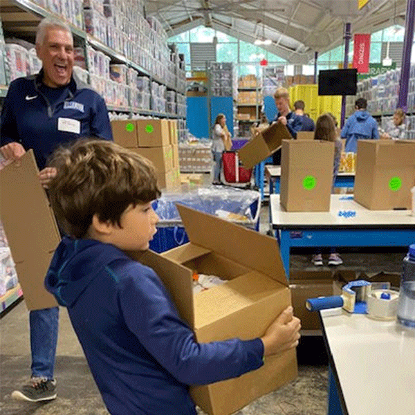 A young boy carries a brown cardboard box in a warehouse