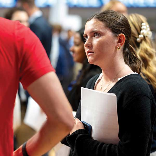 A female student dressed in black holds papers while looking up at someone.