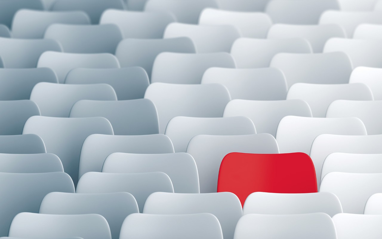 One red chair among many white lecture hall chairs